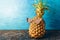 Ripe pineapple in black sunglasses on blue background. The concept of rest in the tropics. Close-up of a fruit with space for co