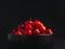 Ripe red acerola cherries fruit in a ceramic bowl with a black background.