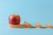 Ripe red apple and yellow measuring tape curles on a blue medical background. Concept of healthy eating, body weight control,