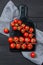 Ripe red cherry tomatoes in different size on a dark marble cutting board on black wooden table, top view