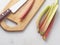 Ripe rhubarb stems and some utensils upon wooden board.