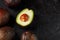 Ripe sliced Hass Avocado with a bone on a black textured background.