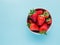 Ripe strawberries forest fruits in white bowl on blue table. Fresh strawberry concept, top view.