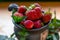 Ripe strawberries lie in a brown mug along with mint leaves on a wooden table among mint leaves