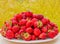 Ripe strawberries on a white plate. Lots of red berries. Blurred green and yellow background