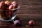 Ripe sweet plum fruits in glass bowl near with scattered plums on dark moody wood table background, hard light, copy space