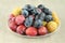 Ripe yellow, blue and pink plums in white plate on linen cloth. Closeup