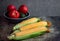 Ripe yellow ears of corn on a dark background and red tomatoes in a dark cup