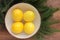 Ripe yellow lemons in a bowl on wooden table decorated with Christmas tree branches. Fresh citrus fruits on wood background.