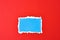 Ripped blue paper torn edge sheet on a red background. Template with piece of color paper