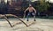 Ripped handsome guy working out with battle ropes while wearing a workout mask, battle ropes