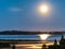 Rising full golden Moon over Umea river delta, summer night with clear skies and tiny white fog over water and coast line. Pine