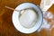 Rising yeast dough with wooden spoon in white enamel metal bowl