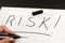 RISK inscription on white. Hand with a black marker writes the word risk on a white piece of paper. Close-up.