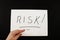 RISK inscription on white. Hand points to the word `risk` written on a white piece of paper.