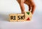 Risk symbol. Wooden cube with word `risk`. Businessman turns the wooden cube, changes the direction of an arrow down or up.