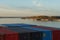 River barges and tug boats moored near container terminal on the Columbia river surrounded by trees and bushes under blue sky.