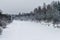 River covered with ice and snow from the forested shores and cloudy sky.