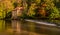 A river crosses a weir, with a background of a house & autumn trees