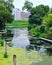 river flowing in the city, duckweed on the river, buildings along the river, boats parked on the water, wooden poles in the water