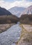 The river flows in a mountain valley between the ridges in autumn against the backdrop of rocky mountain cliffs