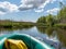 The river from a green fisherman`s rubber boat, calm river water with reflections and bright green vegetation on the shore