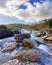 River landscape with large granite rocks washed by running water, clouds in the sky and green plants. Photo wide angle, long