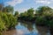 A river in a rural area with banks overgrown with greenery in summer