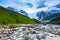 From the river shore, covered with stones, opens view on fantastic glacier and steep rocky mountains with green meadows.