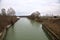 River with the sky and the trees at the edge of it casted in the water in the italian countryside in winter