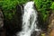 The river stream flows like a stormy waterfall from the rocky slope of the mountain overgrown with small shrubs