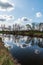 River with trees and sky with clouds mirroring on waterground