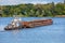 A river tugboat with an empty rusty barge goes crosses a wide river