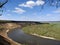 Riverbend in deep spring forest with green trees on the bank of the river and sands under blue sky