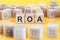 ROA - return on assets - acronym on wooden cubes on yellow background. concept