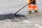 A road builder collects fresh asphalt on part of the road and levels it for repair in road construction.