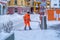 Road cleanup worker in bright orange coat clearing up snow from the road at a street in St. Moritz, Switzerland