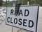 A `Road Closed` sign at a roadblock, with a weight over the top of it.