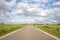 Road in countryside, perspective, under cloud sky and green meadows and a faraway straight horizon