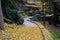 Road cut into the slope. above and below the road is a stone dry wall. nature trail through the autumn park with a drain and a met