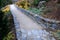 Road cut into the slope. above and below the road is a stone dry wall. nature trail through the autumn park with a drain and a met