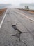 Road damage. Cracked asphalt in rural road in morning mist