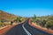 Road with dark tarmac leading between hills at Karijini National Park Australia