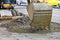 A road excavator bucket pours concrete gravel at a construction site. Close-up