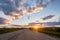 Road in a field at sunset with clouds