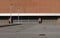 A road in front of a brown and white commercial building with closed entry shutters and street poles. Street lamps and a parking l