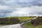 Road goes far away into the distance, horizon, few cars, green field and forest, cloudy blue sky background