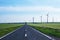 Road going forward with wind turbines on its sides and into the distance, on blue skies. Concept for sustainable energy solutions.