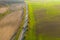 Road between green field and cultivated ground with yellow trees at sunset in autumn. Aerial view on speedway or trees alley..