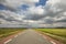 Road in Holland with red cycle path on both sides, perspective, under heavy dark threatening cloudy skies and between green